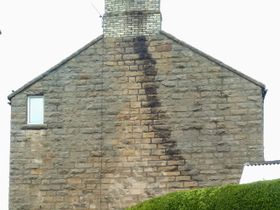 Clear to see that the chimney cavity from living room is performing poorly, the coolness of the stone allows the tars, condensation and soot to condense out onto the porous sandstone, and leach though.  The soot and tar buildup will increase until either a chimney fire will occurr, or it becomes so restricted that copious smoke and CO are produced, much of which will enter the house and endanger the occupants.  A chimney liner is required, after a thorough clean out of the chimney void, to contain any fumes, make the appliance perform more efficiently by retaining heat which creates the 'draw', make the appliance perform cleaner, and make the whole system safe.